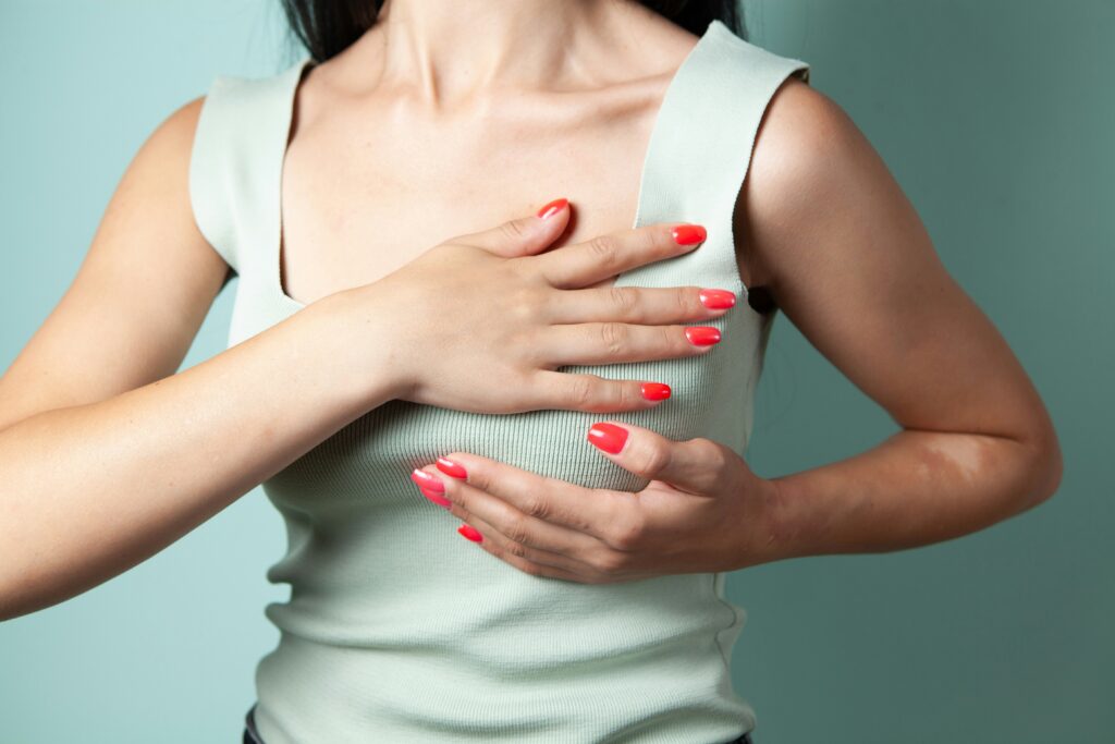 Woman performing a breast self-exam, pressing her chest with both hands in a calm, upright pose.