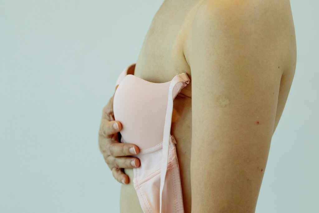 Side view of a person wearing a light pink bra, with one hand resting over the cup against the chest