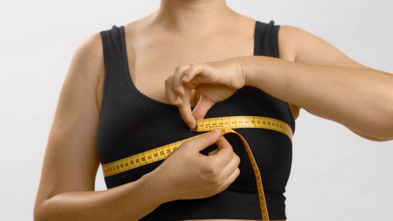 Person wearing a black sports bra measures their chest with a yellow measuring tape wrapped around the bust area