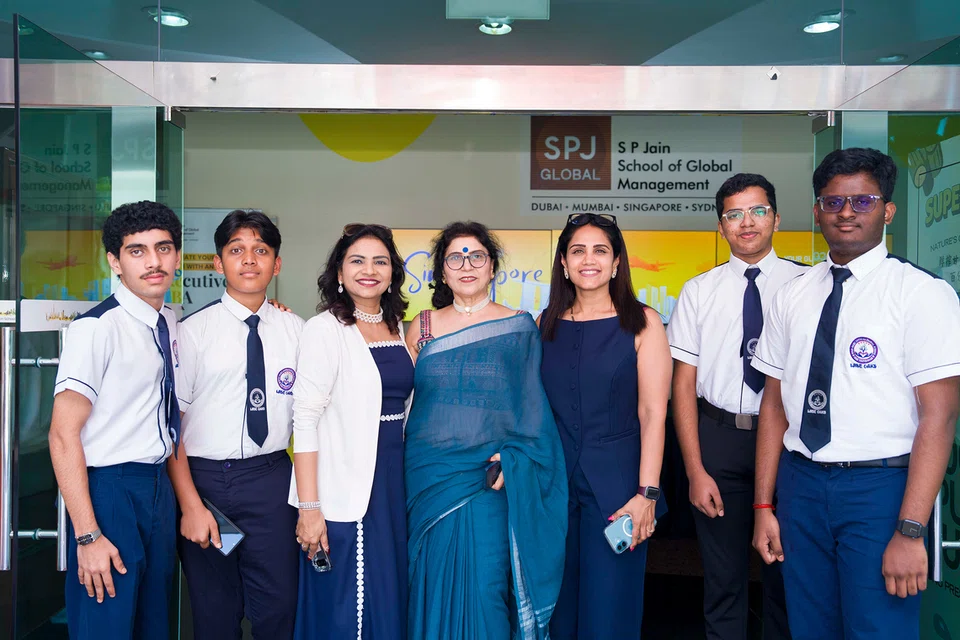 Group of seven people posing in front of the SP Jain School of Global Management entrance sign.