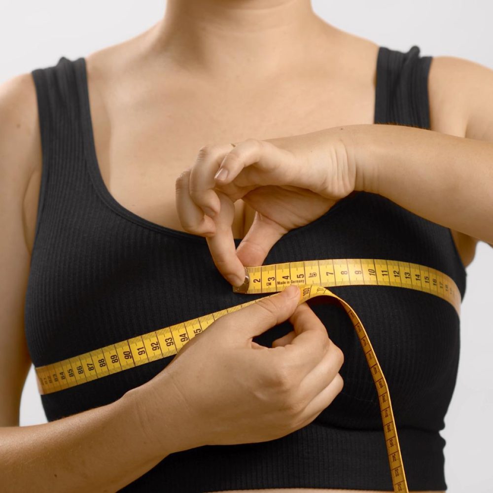 Person wearing a black sports bra measures their chest with a yellow measuring tape wrapped around the bust area